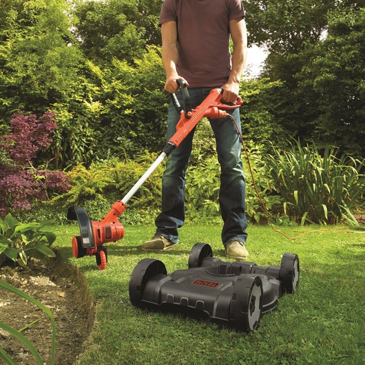 BLACKDECKER ST5530CMCAK lawn trimmer and mower in use on grass in garden, red and black design.