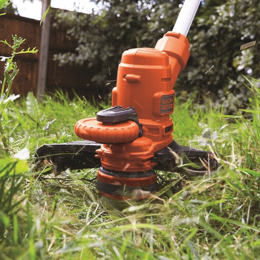 Photo of BLACK+DECKER ST5530CMCAK orange grass trimmer in use cutting tall green grass.