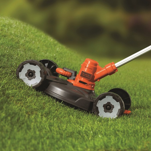 BLACKDECKER ST5530CMCAK orange and black lawn mower cutting grass, side angle.