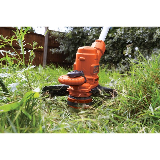 Photo of BLACK+DECKER ST5530 orange grass trimmer in use cutting tall grass outdoors.