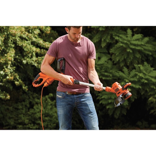Photo of a person holding a BLACKDECKER ST5530 electric grass trimmer with orange and black design, outdoor use.
