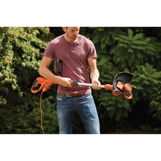 Photo of person holding BLACKDECKER ST5530 orange electric grass trimmer outdoors.
