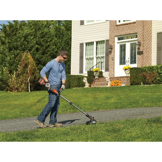 BLACK+DECKER STB3620L cordless grass trimmer in use on lawn near house