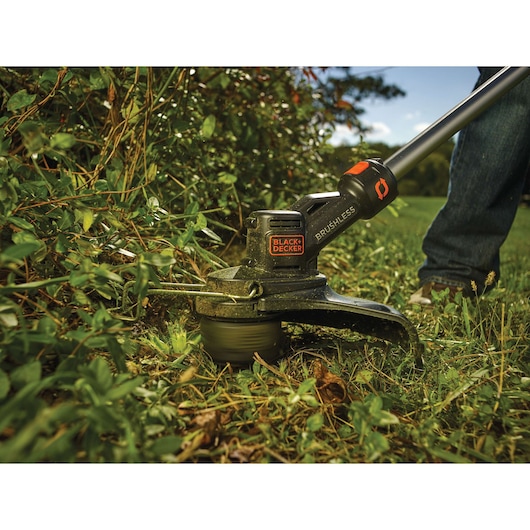 BLACKDECKER STB3620L brushless string trimmer cutting grass outdoors, close-up view.