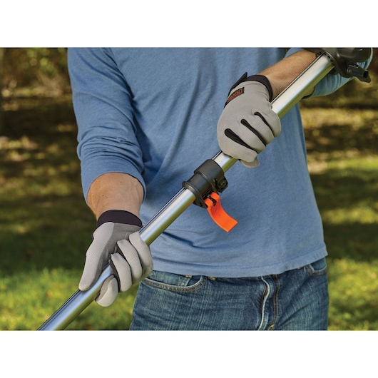 Photo of person wearing gloves adjusting BLACKDECKER STB3620L pole outdoors, focusing on handle and latch.
