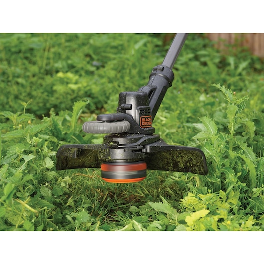 BLACKDECKER STC1820EPC grass trimmer close-up in use on tall green vegetation outdoors.