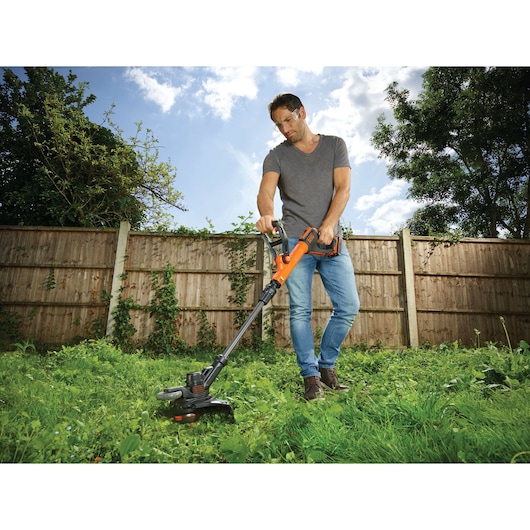 Photo of BLACKDECKER STC1820EPC string trimmer being used outdoors on tall grass, orange and black tool.