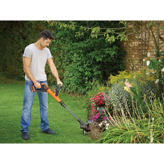 BLACKDECKER STC1820PC grass trimmer used in a garden for edging lawn near flower beds.