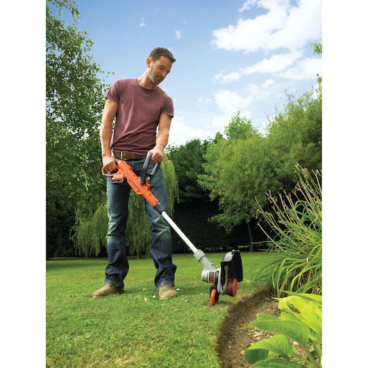 BLACKDECKER STC1820 grass trimmer in use on garden lawn, orange and grey design, photography outdoors