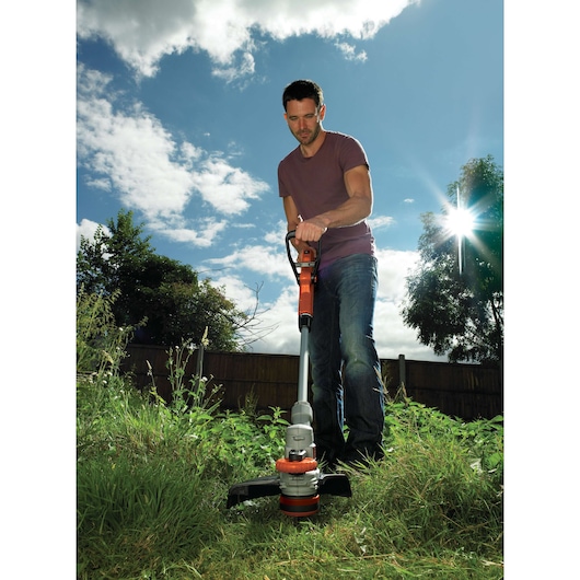Photo of BLACKDECKER STC1820 grass trimmer in use outdoors cutting tall grass.