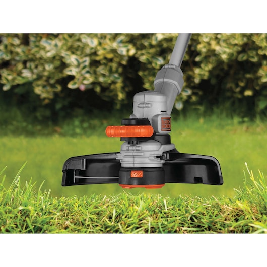 Photo of BLACK+DECKER STC1820 grass trimmer head close-up on lawn with orange and black handle detail.