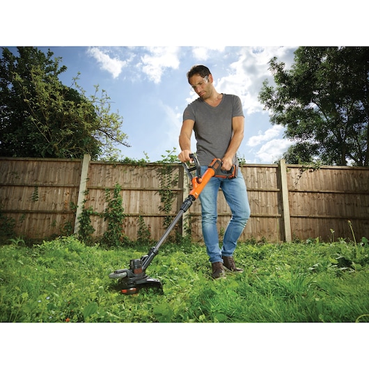 BLACKDECKER STC1840PC cordless grass trimmer used outdoors, orange and black design, yard setting.