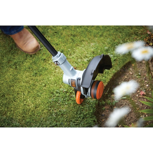 BLACKDECKER STC1840PC grass trimmer in use edging lawn near flower bed, close-up outdoor view.