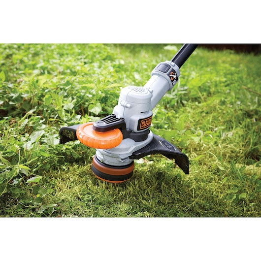 BLACKDECKER STC1840PC grass trimmer close-up in use on lawn, orange and black cutting head visible.