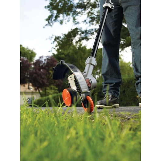 BLACKDECKER STC1840PC grass trimmer in use, close-up outdoor view showing orange wheels and cutting head