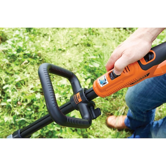 Photography of BLACKDECKER STC1840PC grass trimmer handle in use, orange and black, outdoor setting.
