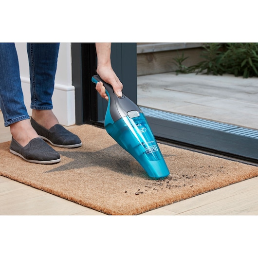 BLACKDECKER WDC215WA handheld vacuum cleaning dirt from a doormat near a door.