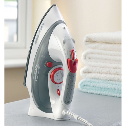 BLACK+DECKER XT2030 steam iron with grey and red accents shown upright on an ironing board, stacked towels in background.