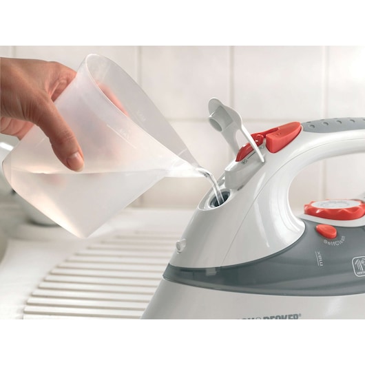 Photo of BLACKDECKER XT2030 steam iron being filled with water from a plastic pitcher, close-up view.