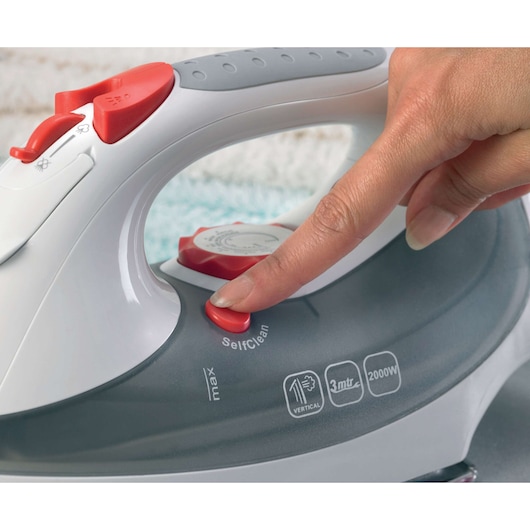 BLACKDECKER XT2030 steam iron close-up with finger pressing red SelfClean button, white and gray body.