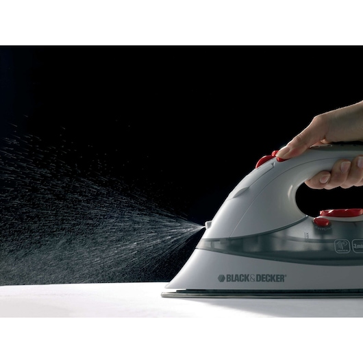 BLACK+DECKER XT2030 steam iron spraying water, side angle, hand pressing spray button.