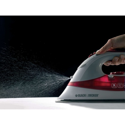 Photo of BLACK+DECKER XT2040 steam iron spraying water, hand pressing button, side view on black background.