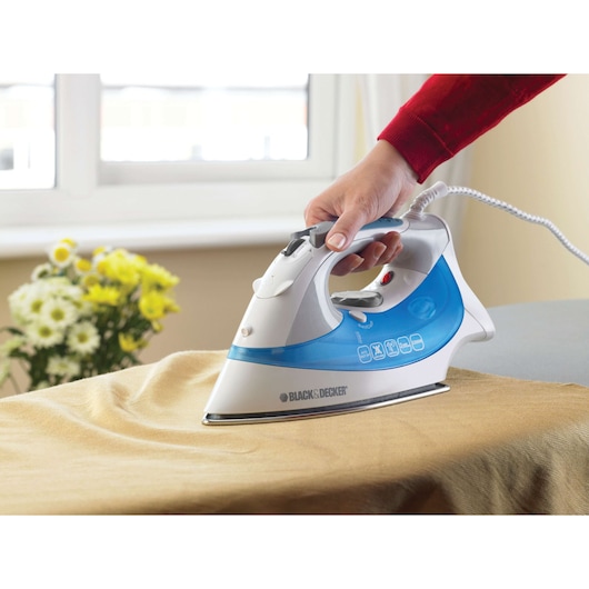 Photo of BLACK+DECKER XT2200CP steam iron with blue and white design being used to iron a tan fabric.