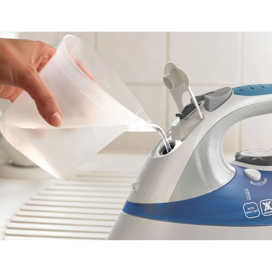 BLACKDECKER XT2200CP steam iron close-up, water being poured into tank from a clear measuring cup.