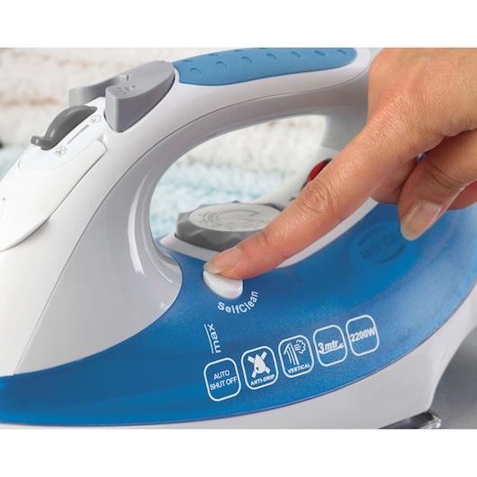 BLACKDECKER XT2200CP steam iron closeup, hand pressing self-clean button, blue and white design, feature icons visible.
