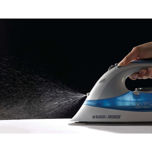 BLACK+DECKER XT2200CP steam iron spraying water, side view, hand pressing button, blue water tank.