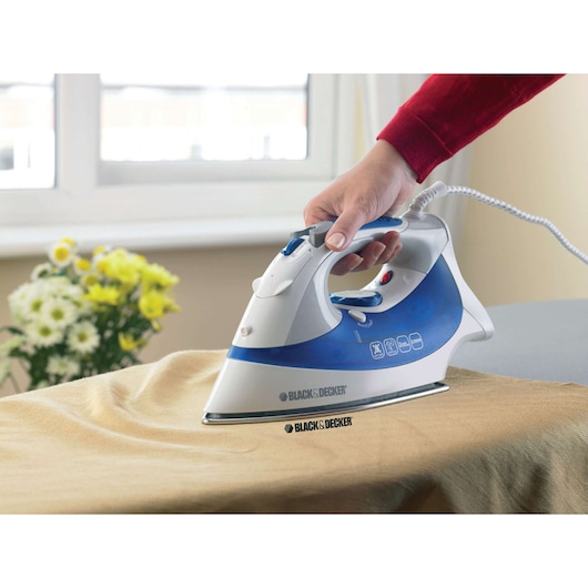 BLACKDECKER XT2200 steam iron, blue and white, side view, ironing beige fabric.